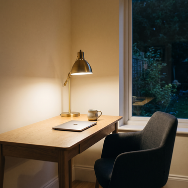 A warm task lamp lit over an oak desk with a closed laptop in an evening home office