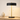 Black disc table lamp on a light wood console with a ceramic vase, shade on