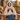 Woman on a cabin porch wearing the beige wearable heated blanket with the hood up