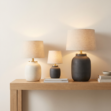 Three lit table lamps of different heights grouped on an oak console against a cream wall
