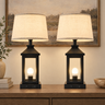 Closeup of black metal lantern farmhouse pair — square to console, both lamps on, clean stems.