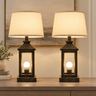 Closeup of black-gold lantern farmhouse pair — square to console, both lamps on, clean stems, gold rub-through.