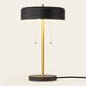Black disc table lamp with a wide shallow black drum shade and gold stem, lamp on