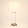 Brushed nickel table lamp with a clear glass cylinder and white fabric shade, lamp on