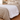 White chunky knit weighted blanket across the foot of a bed with sand linen bedding