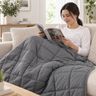 Woman reading on a sofa with the gray weighted throw blanket over her lap and legs